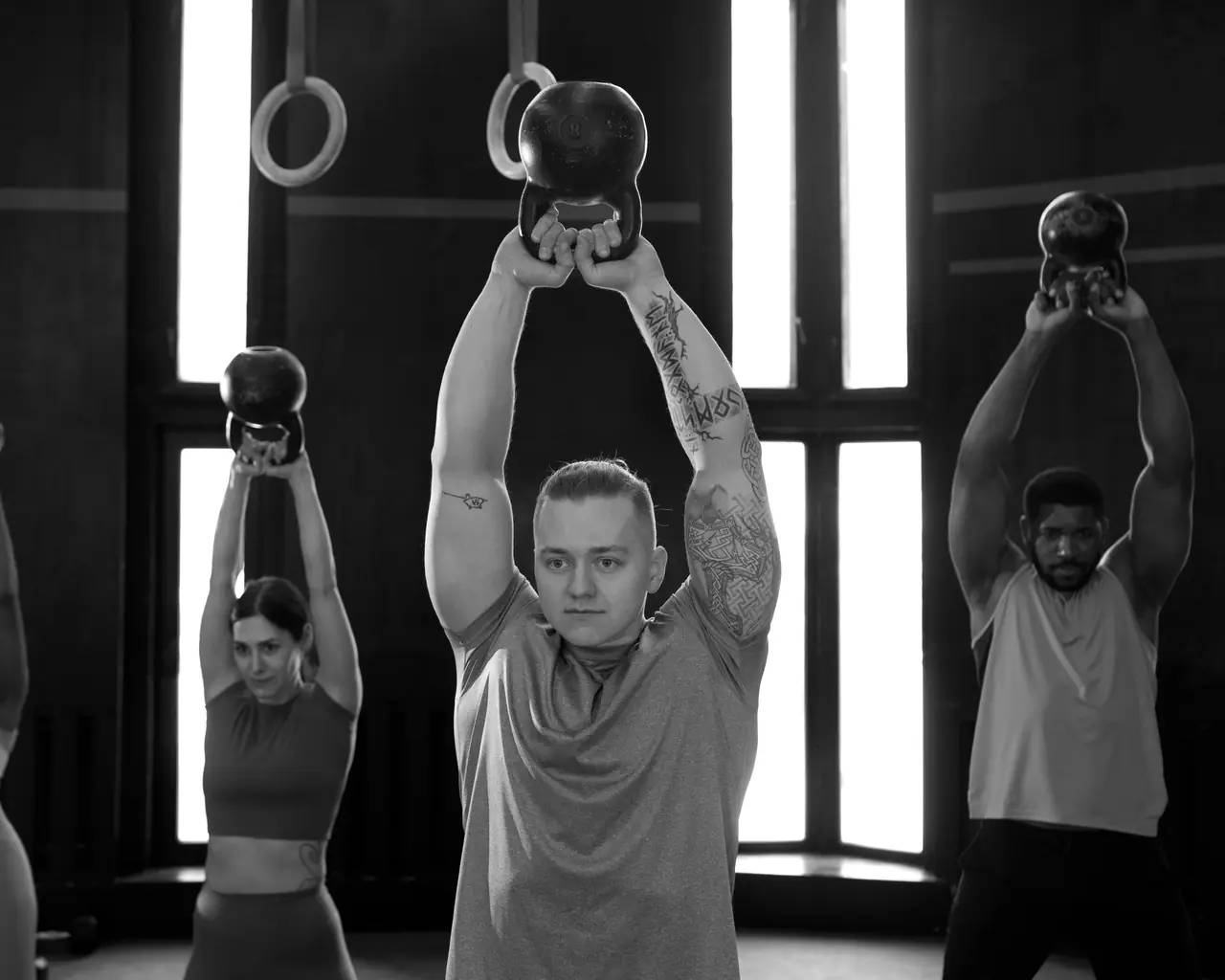 Una classe solleva i kettlebell sopra la testa davanti ai finestroni della sala